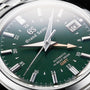 Close-up of the Grand Seiko Hi-Beat GMT Elegance watch, featuring a green dial, time, date window, and Automatic Hi-Beat 36000 GMT with Calibre 9S86 movement.