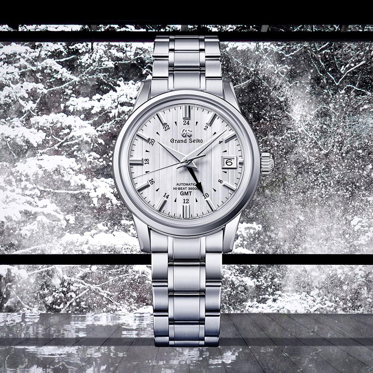 A Grand Seiko Hi-Beat GMT Elegance stainless steel wristwatch with a white textured dial, shown against a snowy window backdrop.