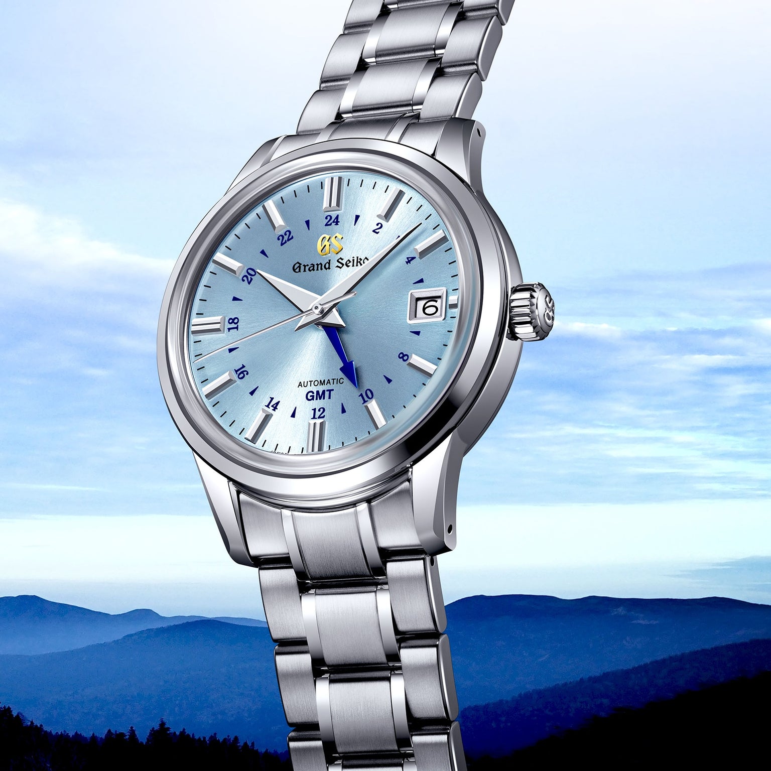 The Grand Seiko Automatic GMT Elegance watch, featuring a light blue dial and Calibre 9S66 movement in silver, is displayed against a mountain landscape background.