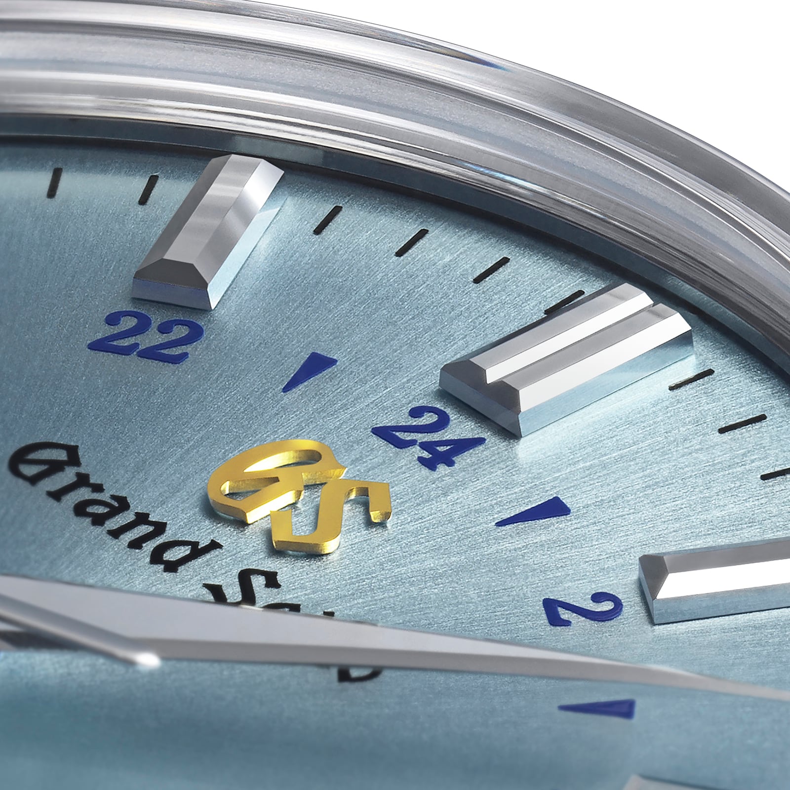 Close-up of a Grand Seiko Automatic GMT Elegance watch face with a light blue background, metallic hour markers, blue numerals, and a gold GS logo at the center, powered by the Calibre 9S66 movement.