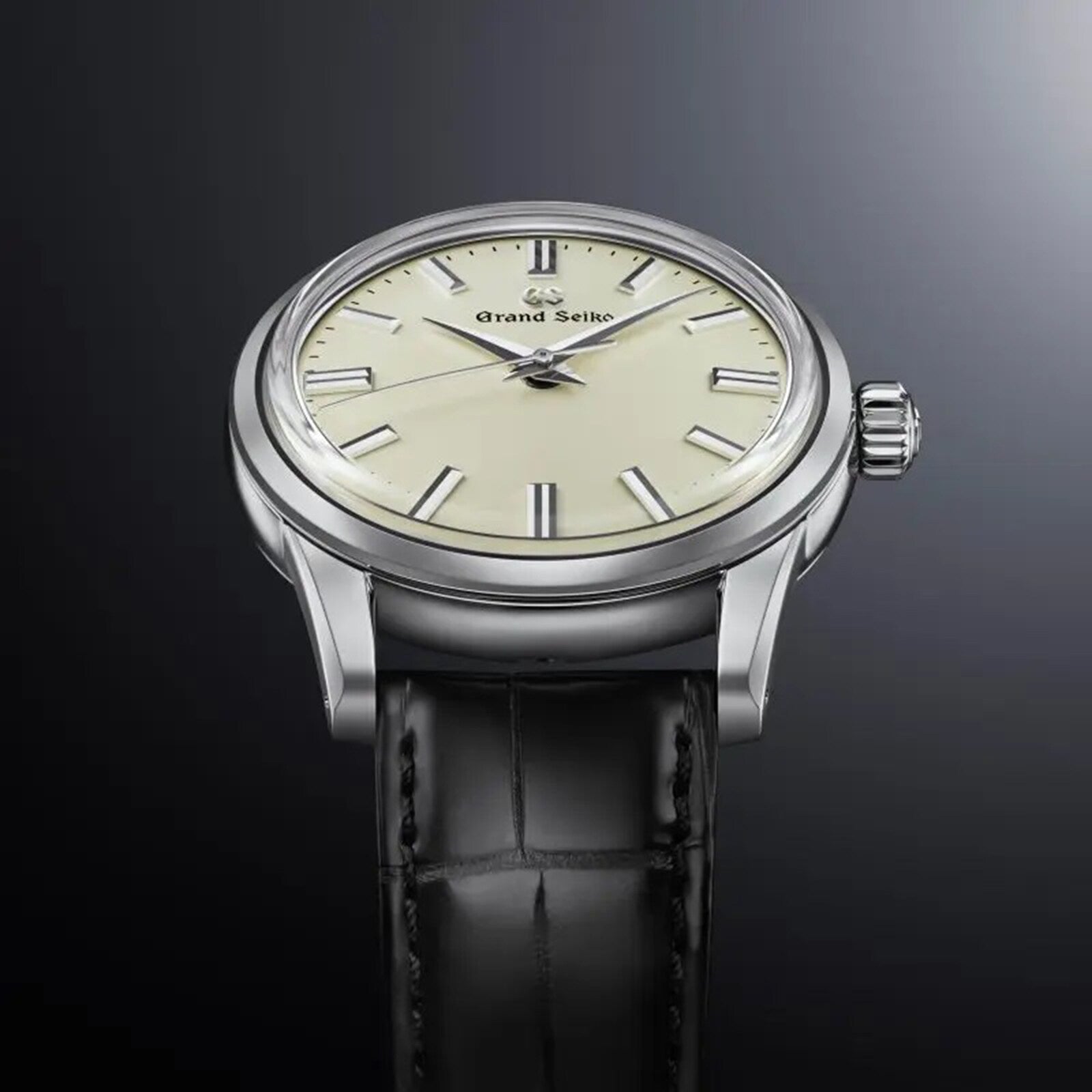 The Grand Seiko Manual Elegance wristwatch, featuring a cream dial, silver hour markers, and black leather strap, is displayed against a dark gradient background and showcases the precision 9S64 mechanical calibre movement.