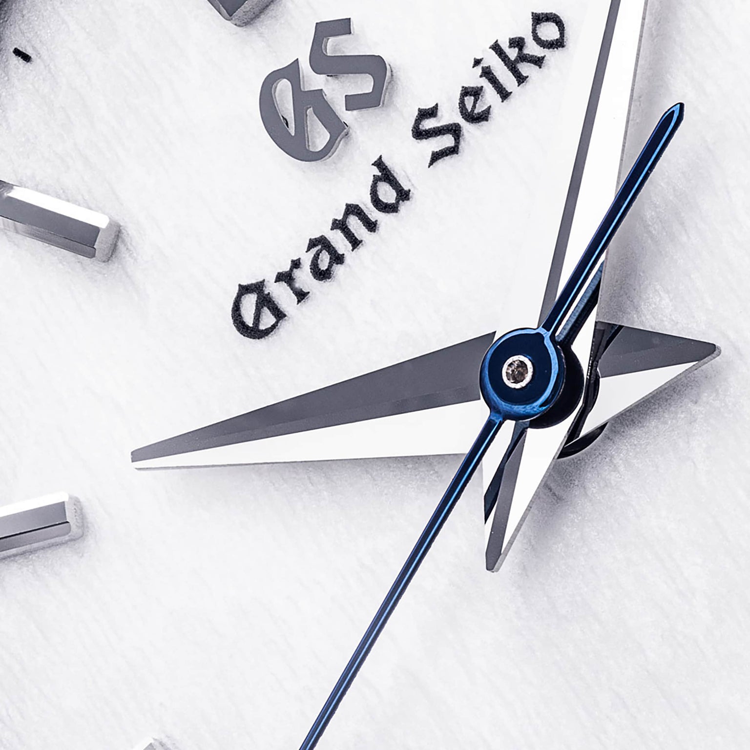 Close-up of the Grand Seiko Quartz Heritage watch face with a textured white dial, silver hour and minute hands, blue second hand, and the Grand Seiko logo.