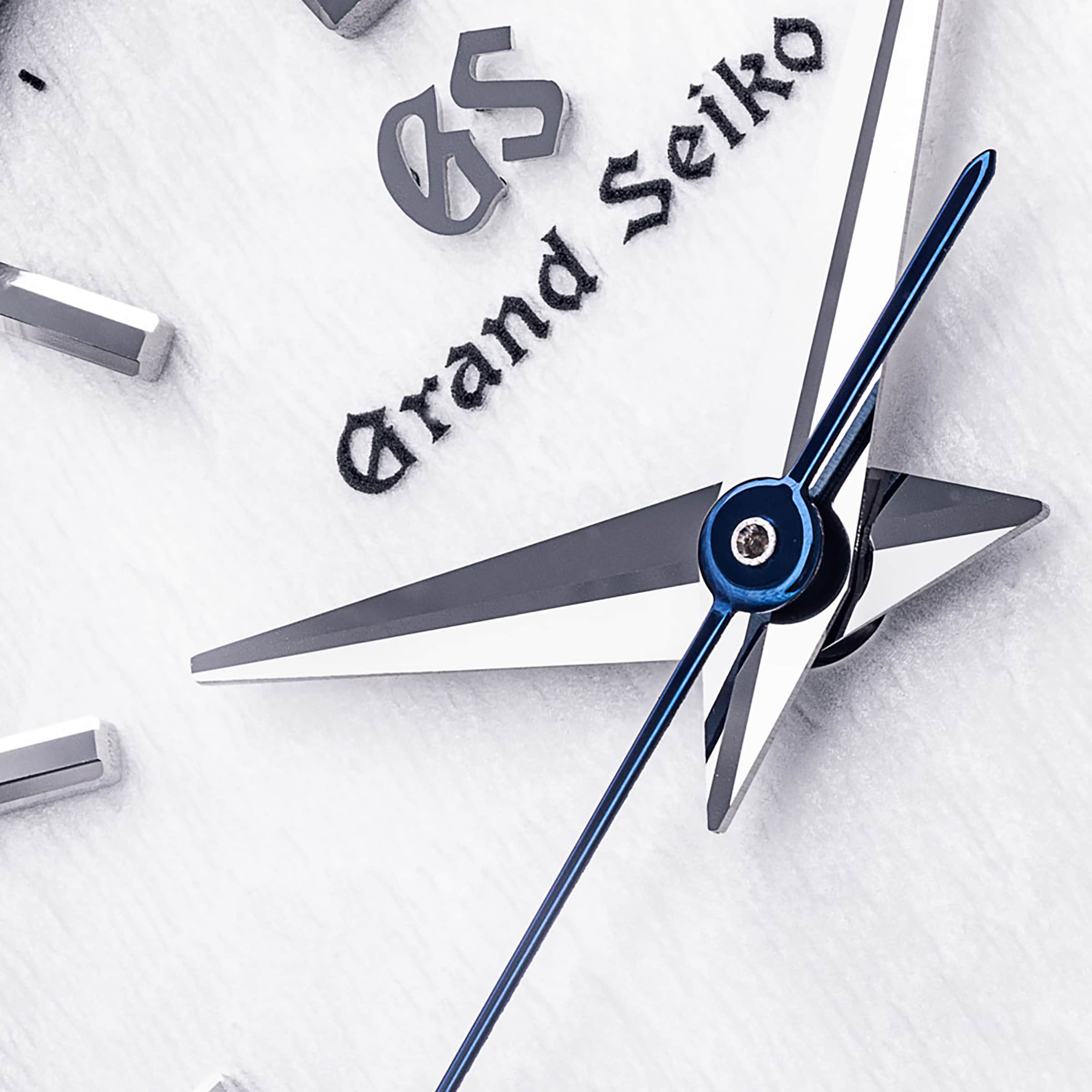 Close-up of the Grand Seiko Quartz Heritage watch face with a textured white dial, silver hour and minute hands, blue second hand, and the Grand Seiko logo.