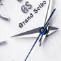 Close-up of the Grand Seiko Quartz Heritage watch face with a textured white dial, silver hour and minute hands, blue second hand, and the Grand Seiko logo.