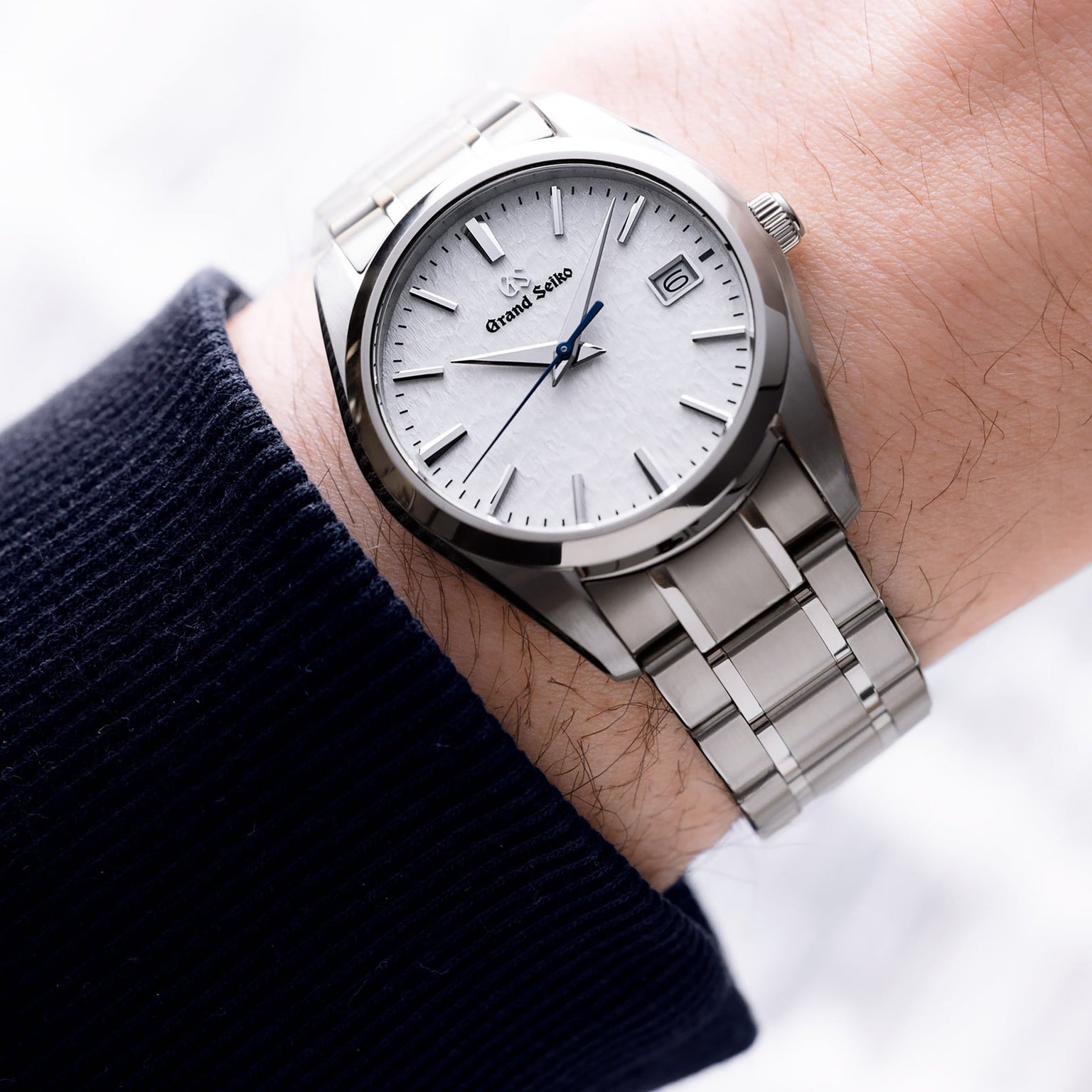A Grand Seiko Quartz Heritage wristwatch with a 37mm titanium case, snowflake dial, date display, and silver indices is worn on a persons left wrist.
