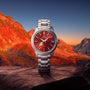The Grand Seiko Spring Drive Elegance, featuring a silver case and red dial, is showcased before a vivid sunset over mountain peaks.