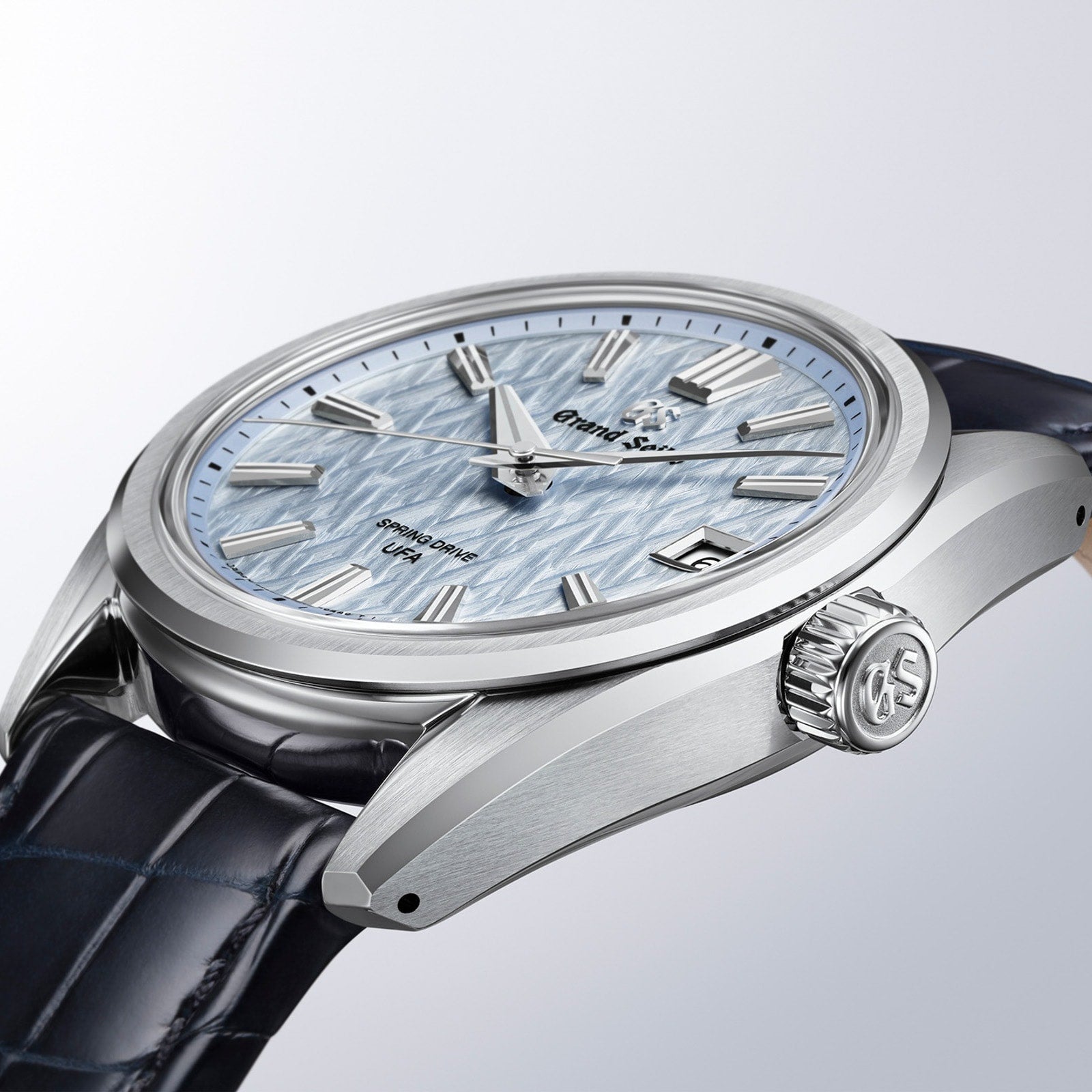 The Grand Seiko Spring Drive U.F.A Evolution 9 is a silver wristwatch featuring a textured light blue dial and a dark leather strap.