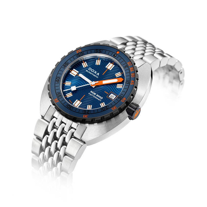 The DOXA Sub 300 Beta Caribbean sports watch features a blue dial with orange accents, a ceramic bezel, and date display on a metal bracelet, shown against a white background.
