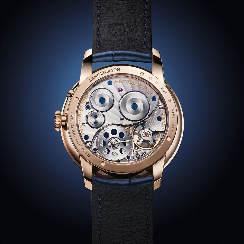 Close-up of Arnold & Son Perpetual Moon 41.5mm Red Gold’s intricate exposed movement, gold casing, and black leather strap.