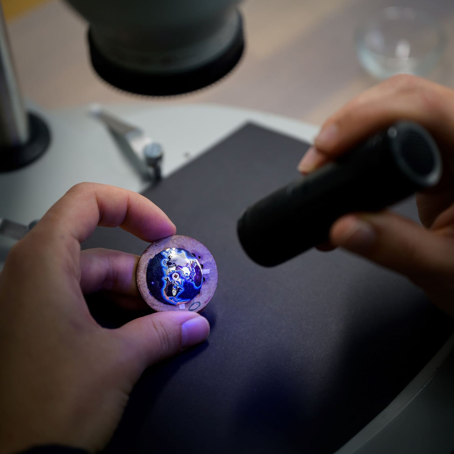 A person shines a flashlight on Globetrotter Steel by Arnold & Son under a microscope, revealing a galaxy pattern.
