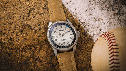 Watch with brown leather strap on a textured surface next to a baseball