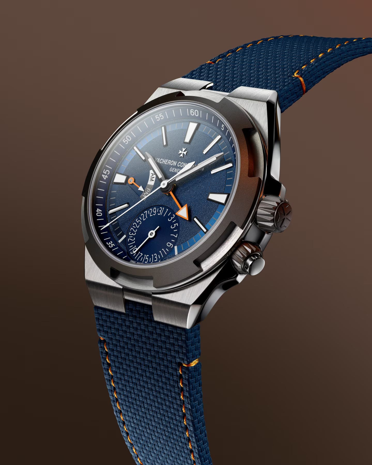 Stainless steel watch with blue dial, dual time zone subdial, orange accents, and blue fabric strap with orange stitching.