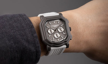A wrist with a gray shirt sleeve and a Gerald Charles Maestro 3.0 Chronograph watch with light gray strap and dark gray bezel, as well as three subdials and a textured gray dial