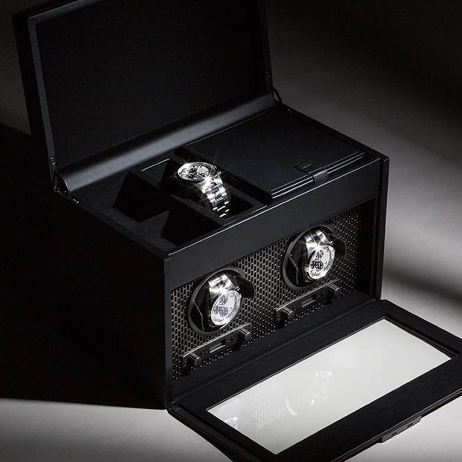 The WOLF Axis Double Watch Winder With Storage, shown in black and illuminated by dramatic lighting, elegantly displays two luxury watches.