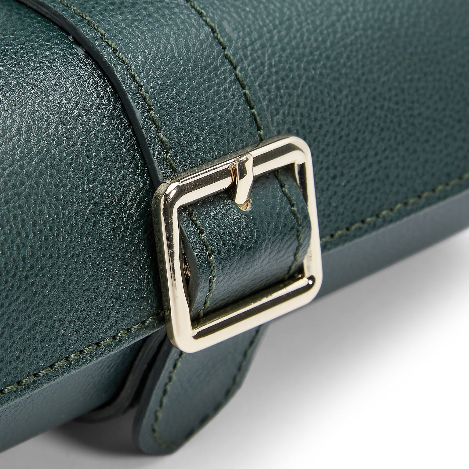 Close-up of a gold buckle on the textured dark green leather strap of the WOLF British Racing Triple Watch Roll.