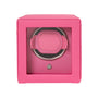 The WOLF Cub Single Watch Winder with Cover features a pink design with a transparent front, showcasing a circular watch holder inside.