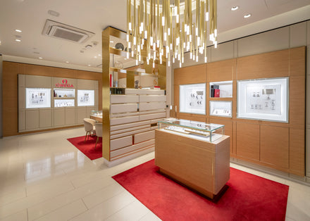 Luxury watch boutique with glass display cases, red carpets, and a modern chandelier overhead.