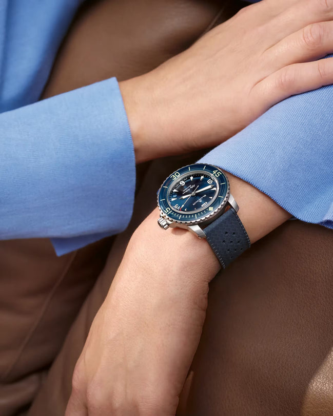 Fifty Fathoms watch with sunburst blue dial and rotating bezel worn on wrist with dark rubber strap.