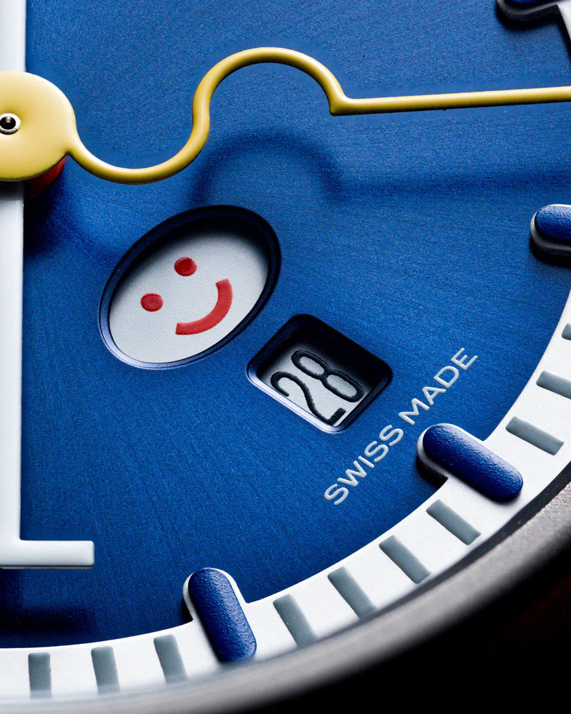 Blue watch dial featuring a smiling face design with red eyes and mouth, yellow hand, and "Swiss Made" text.