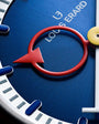 Blue watch dial with red smile-shaped hand and Louis Erard branding visible.
