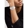 A person in a textured black top rests their chin on their hand, showing a Chanel J12 wristwatch with a white round face and elegant silver accents.