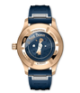 Rose gold pilot's watch with dark blue dial featuring Le Petit Prince illustration, blue rubber strap, and visible case back.
