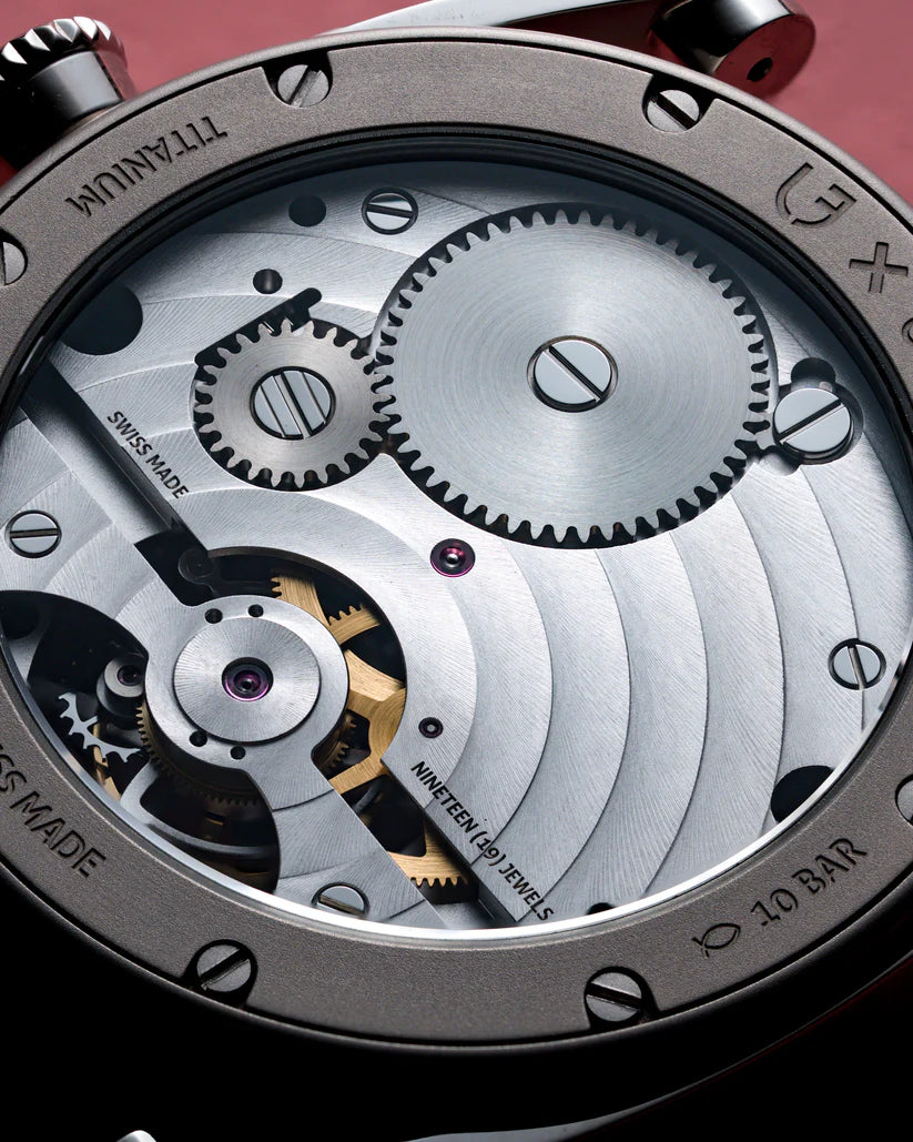 Close-up of watch movement showing tourbillon mechanism with exposed gears, balance wheel, and gold-colored rotor on silvered
