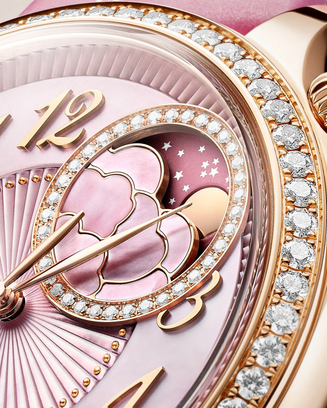 Rose gold watch with pink dial, moon phase complication, crystal diamond bezel, and gold hour markers.