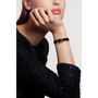 A woman in a textured black long-sleeve top rests her chin on her hand, showcasing the Chanel Première Ribbon—a small, square wristwatch with a black-lacquered dial and black strap—against a plain white background.