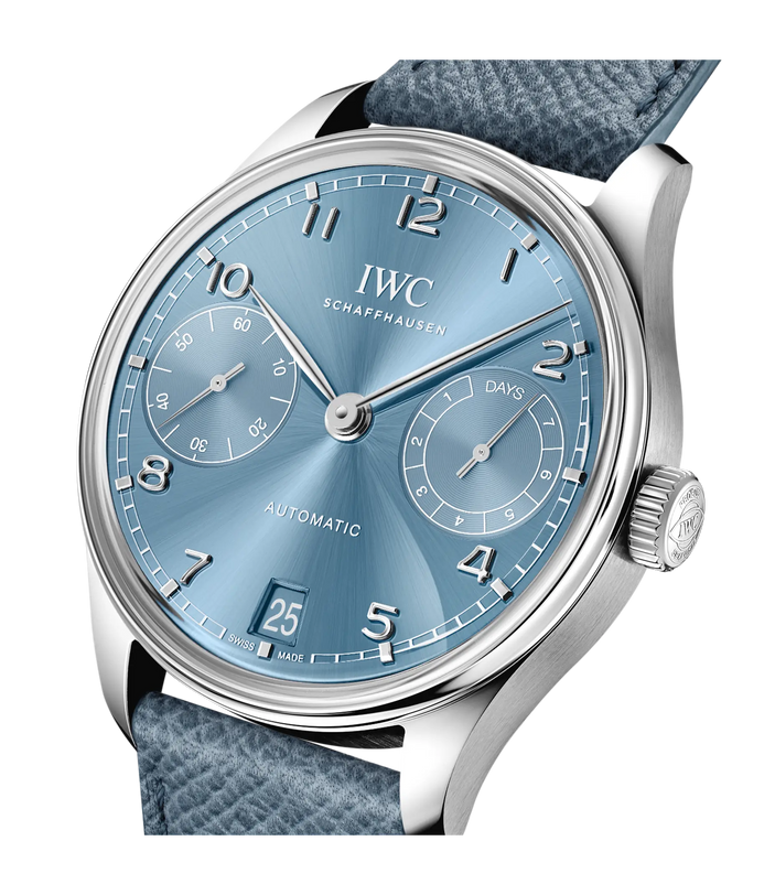 A close-up of the IWC Schaffhausen Portugieser Automatic 42 wristwatch, featuring a blue dial with silver numerals and hands, two subdials, date display, textured blue strap, chronometer precision, and a 7-day power reserve.