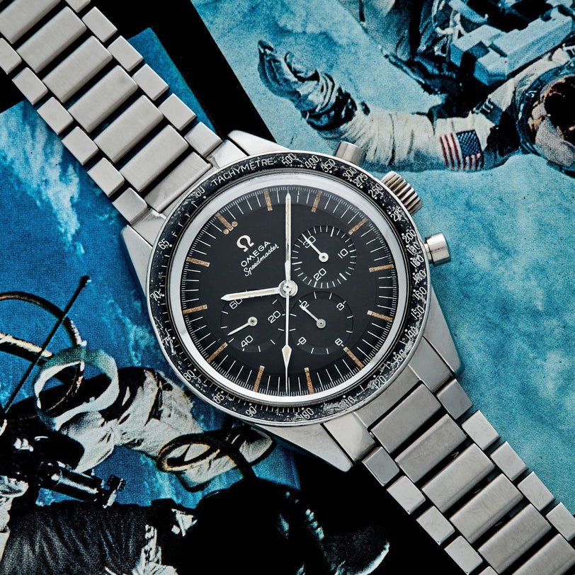 A Watches of Switzerland Speedmaster Ed White watch rests on a magazine page featuring astronauts floating in space.