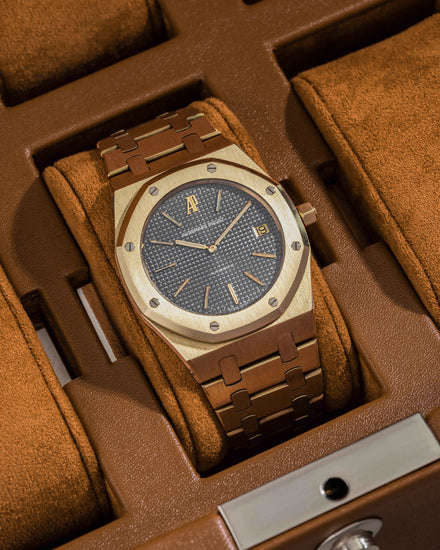 A gold luxury wristwatch with a brown band in a brown suede watch case.
