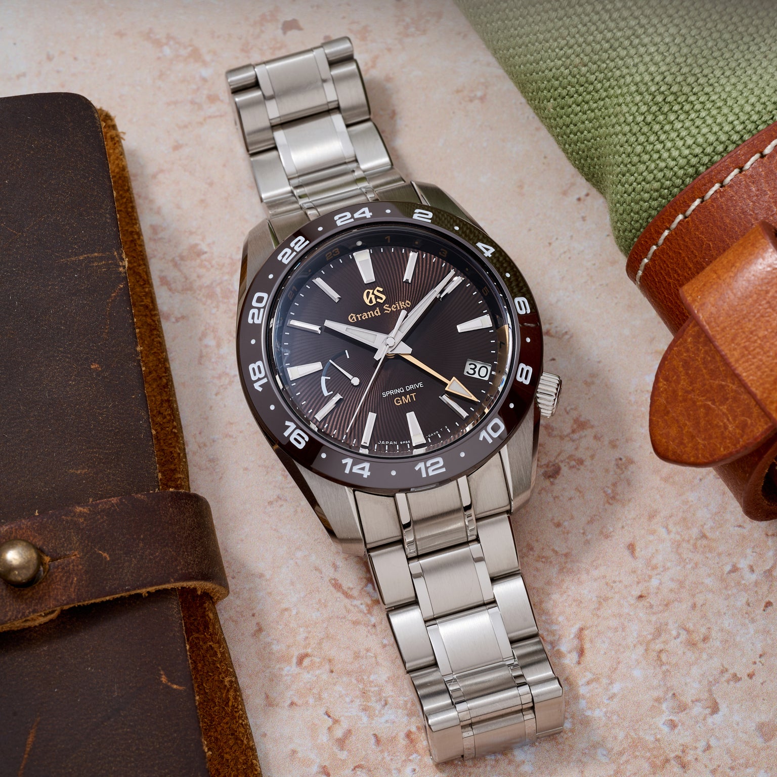 Silver wristwatch with a black dial on a textured surface with leather cases.