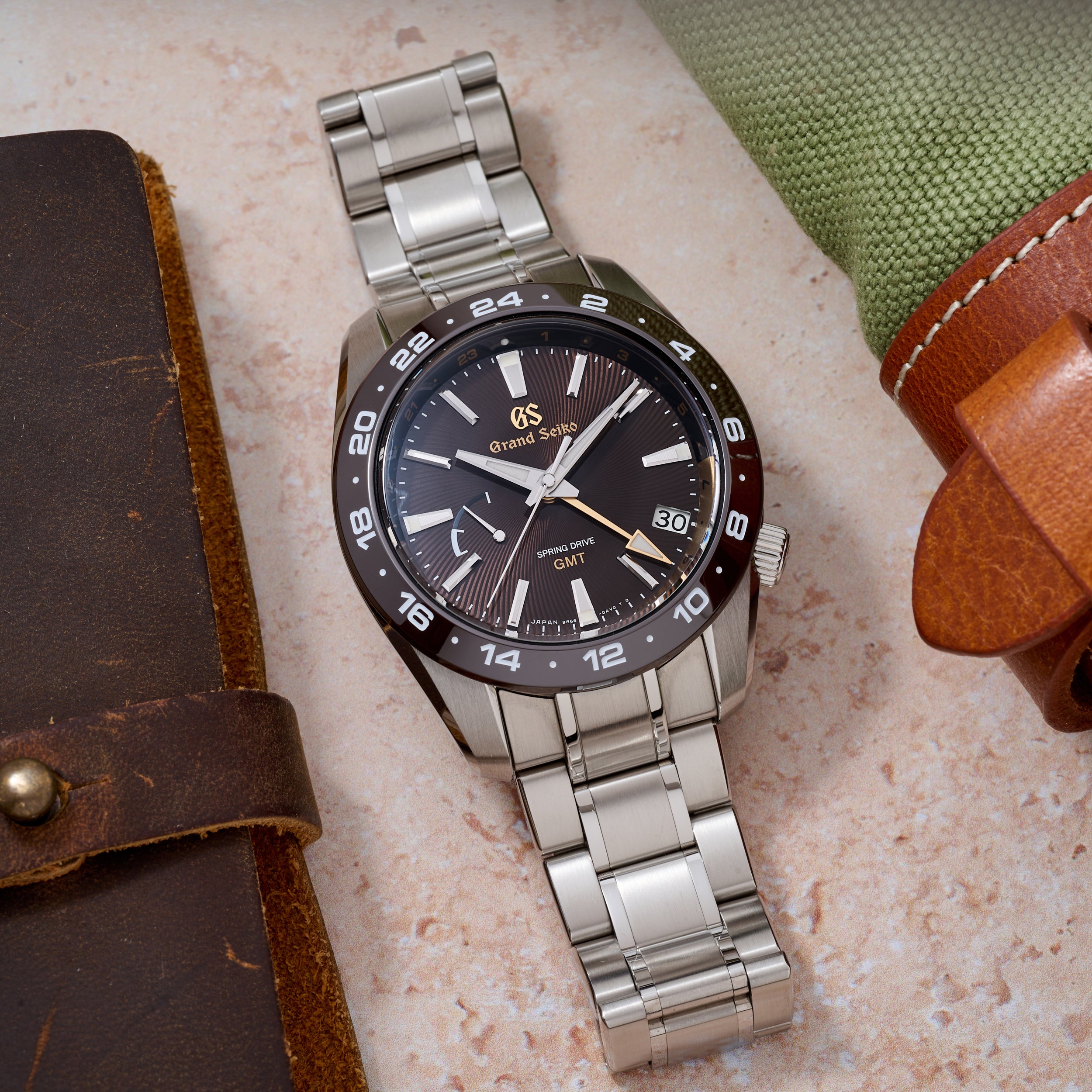 Silver wristwatch with a black dial on a textured surface with leather cases.