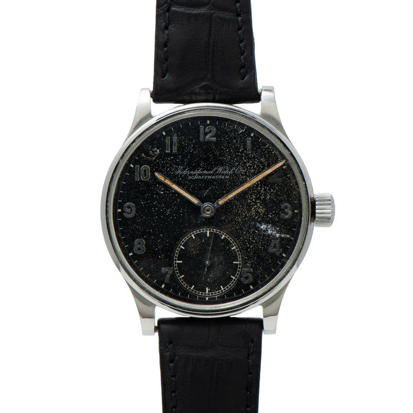 The IWC Schaffhausen Portugieser is a vintage wristwatch featuring a black speckled dial and a black leather strap.