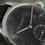 Close-up of an IWC Schaffhausen Portugieser wristwatch featuring a speckled, worn black dial and faded hands.