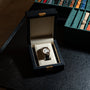 The Lange & Sohne Lange 1 Tourbillon luxury wristwatch is presented in a black display box next to a case of assorted watch straps on a dark table.