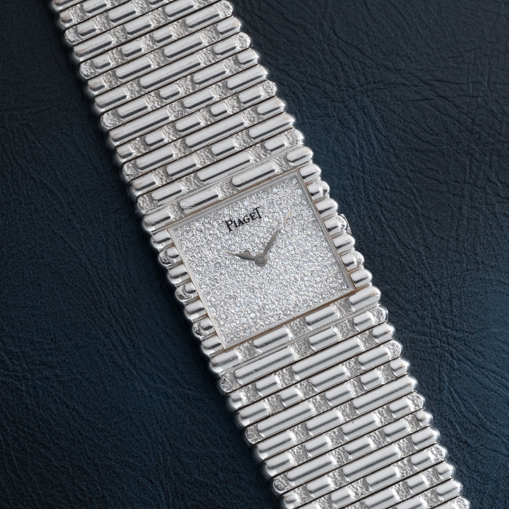 The Piaget Emperador Diamond wristwatch features a diamond-set face and silver linked metal band, displayed elegantly on a dark textured surface.