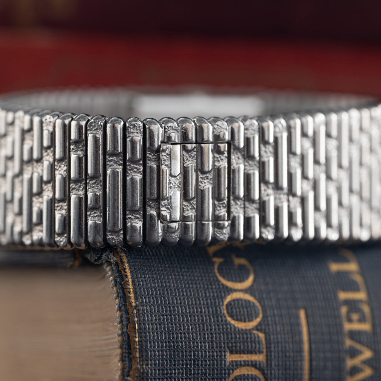 Close-up of the textured silver bracelet of the Piaget Emperador Diamond watch, elegantly resting atop a stack of vintage books.