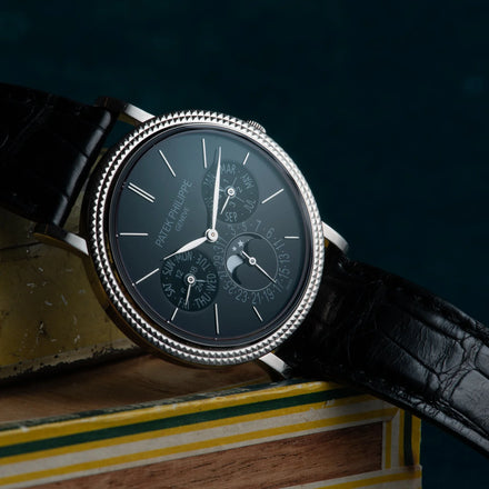 Luxury black Patek Philippe wristwatch with leather strap resting on stacked books against a dark background.