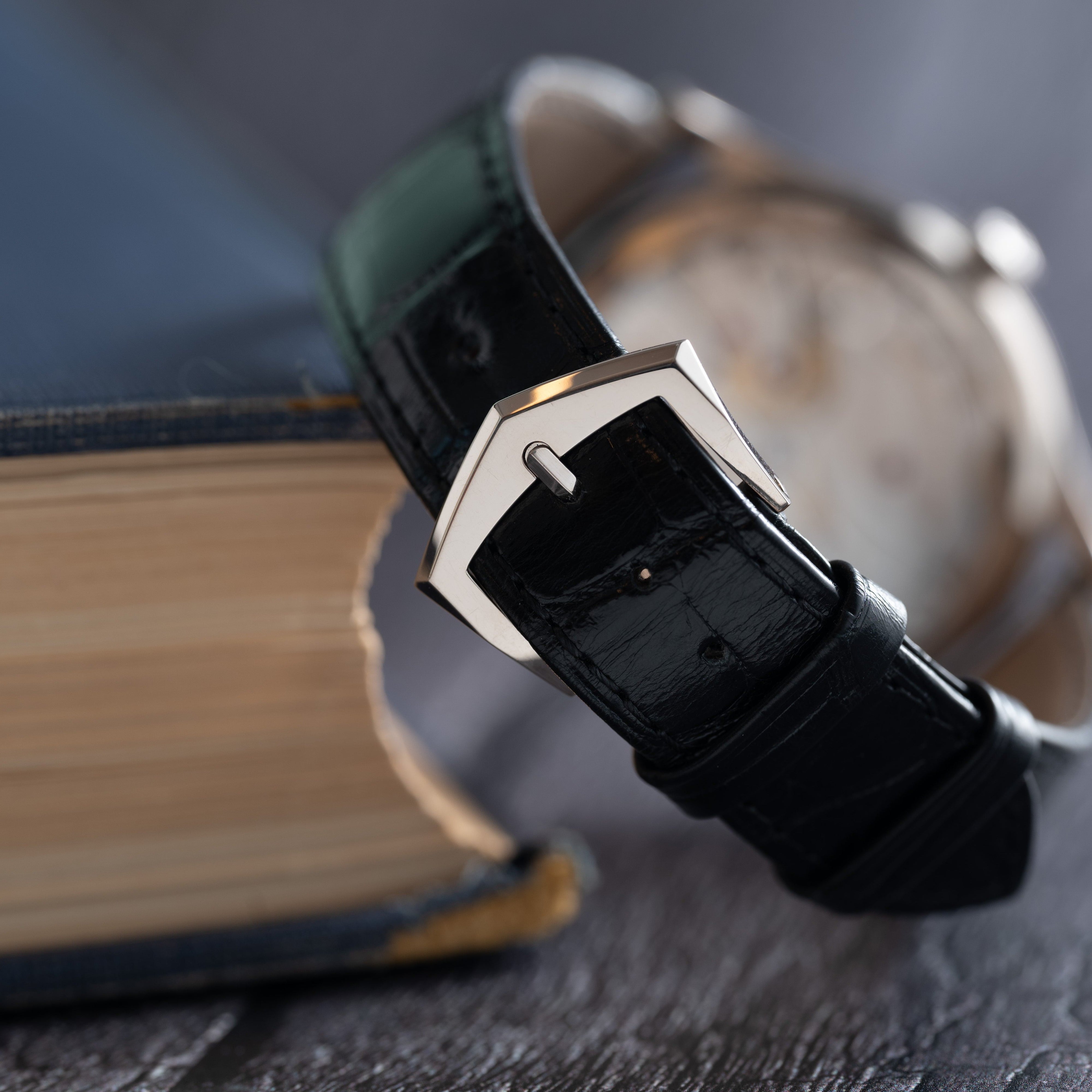 A close-up of the Patek Philippe Calatrava with a black leather strap resting on the edge of an old book.