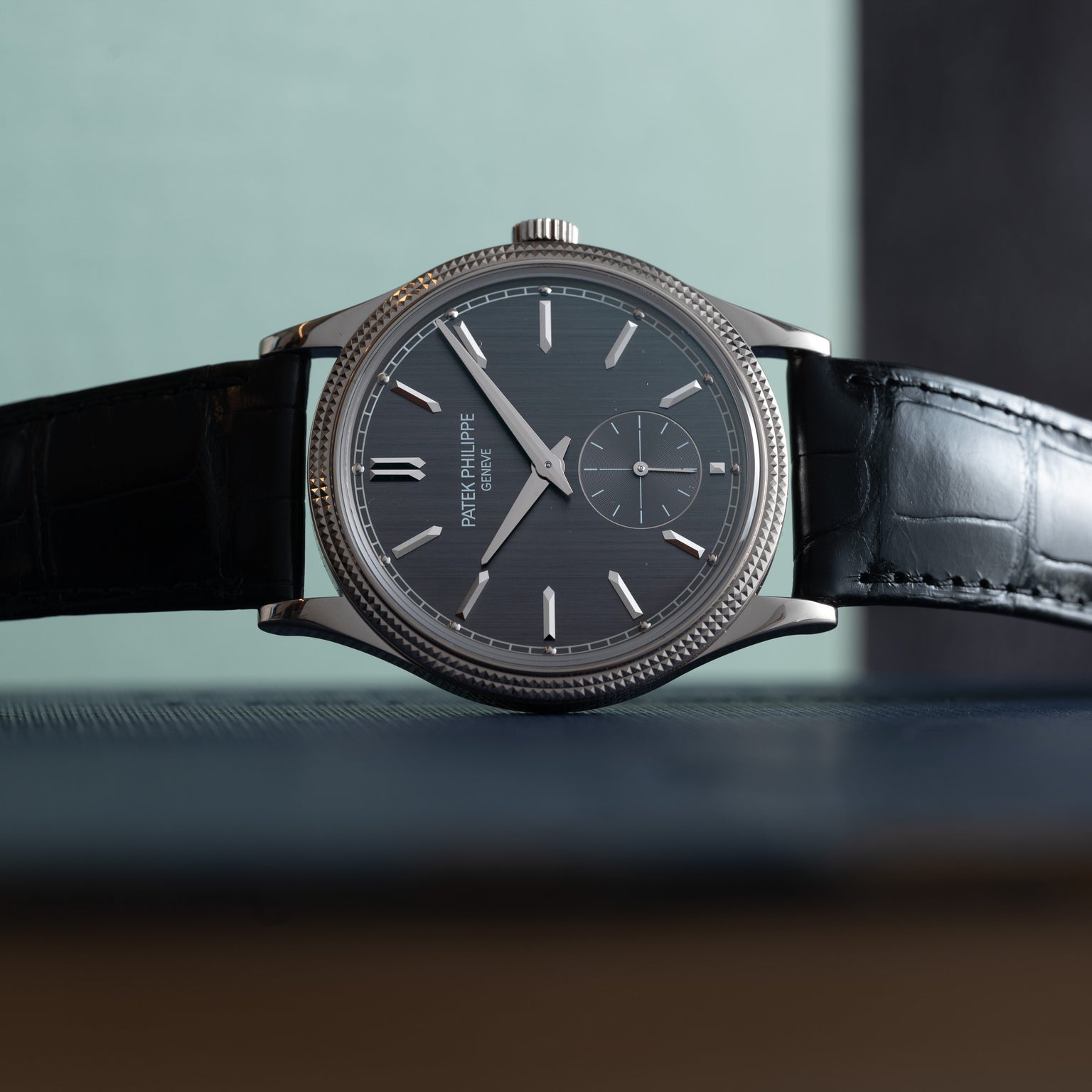 A Patek Philippe Calatrava luxury wristwatch with a black leather strap displayed on its side.