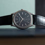 A Patek Philippe Calatrava luxury wristwatch with a black leather strap displayed on its side.