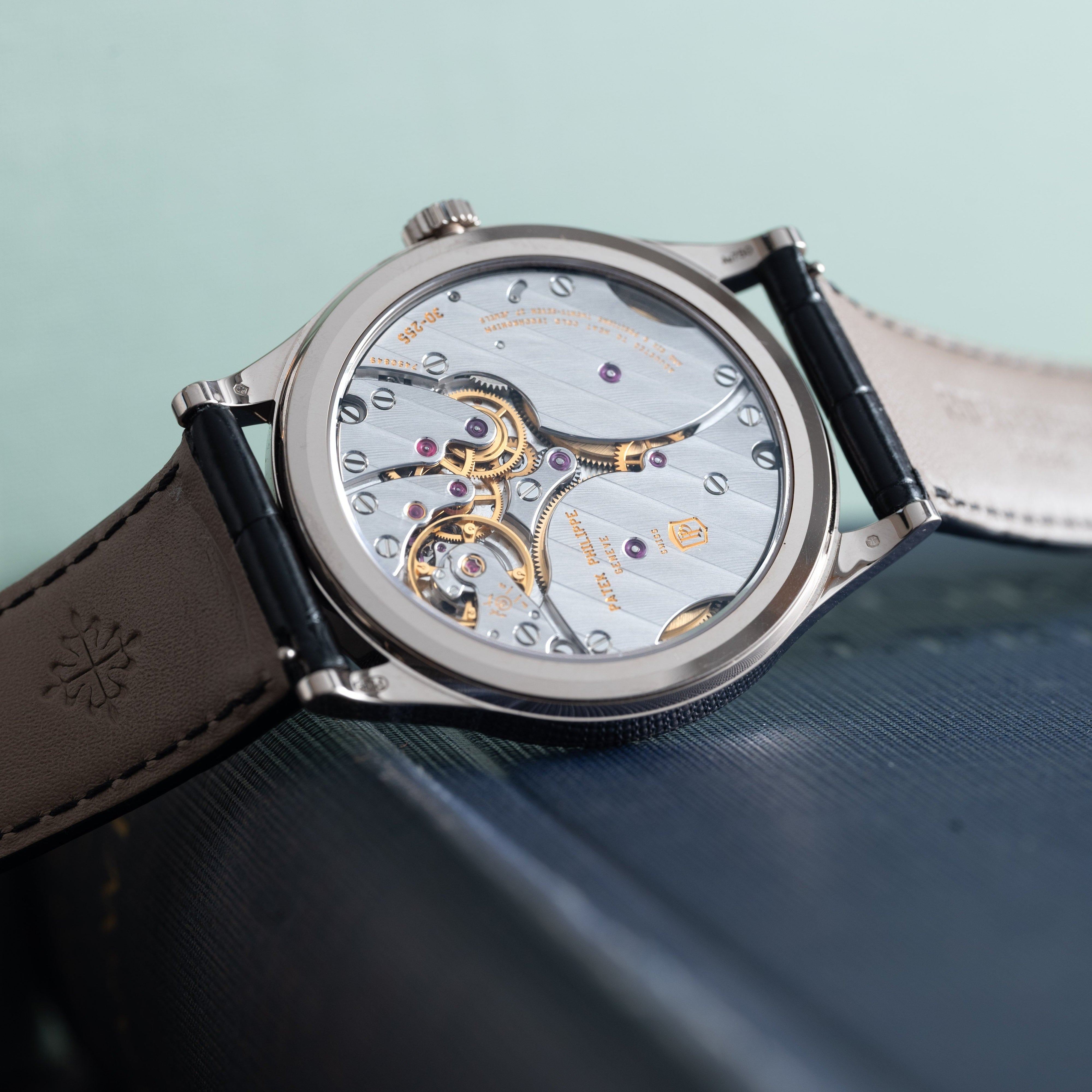 Close-up of the Patek Philippe Calatrava luxury wristwatch with an exposed mechanical movement and leather strap, resting on a book.