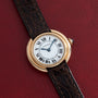 A Cartier Vendome gold wristwatch with a brown leather strap displayed on a red textured background.