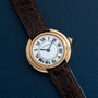 A Cartier Vendome watch with a brown leather strap and Roman numeral dial, displayed on a dark blue surface.