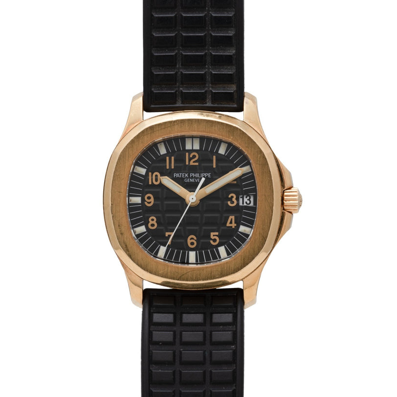A Patek Philippe Aquanaut wristwatch in gold with a black dial, black textured rubber strap, and date display.
