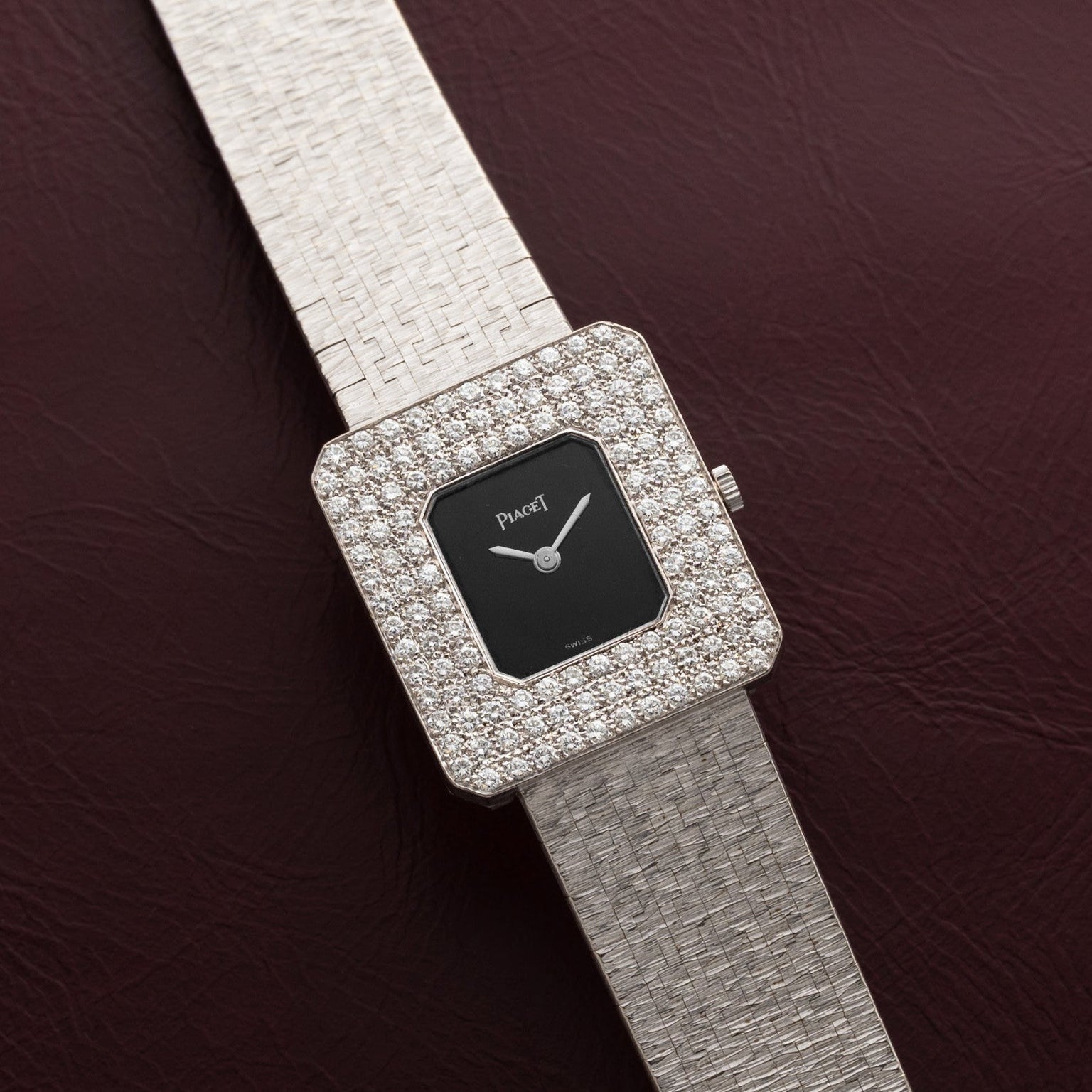 Piaget Onyx Diamond Dress Watch featuring a square face, textured silver band, and diamond-encrusted bezel, displayed on a dark red surface.