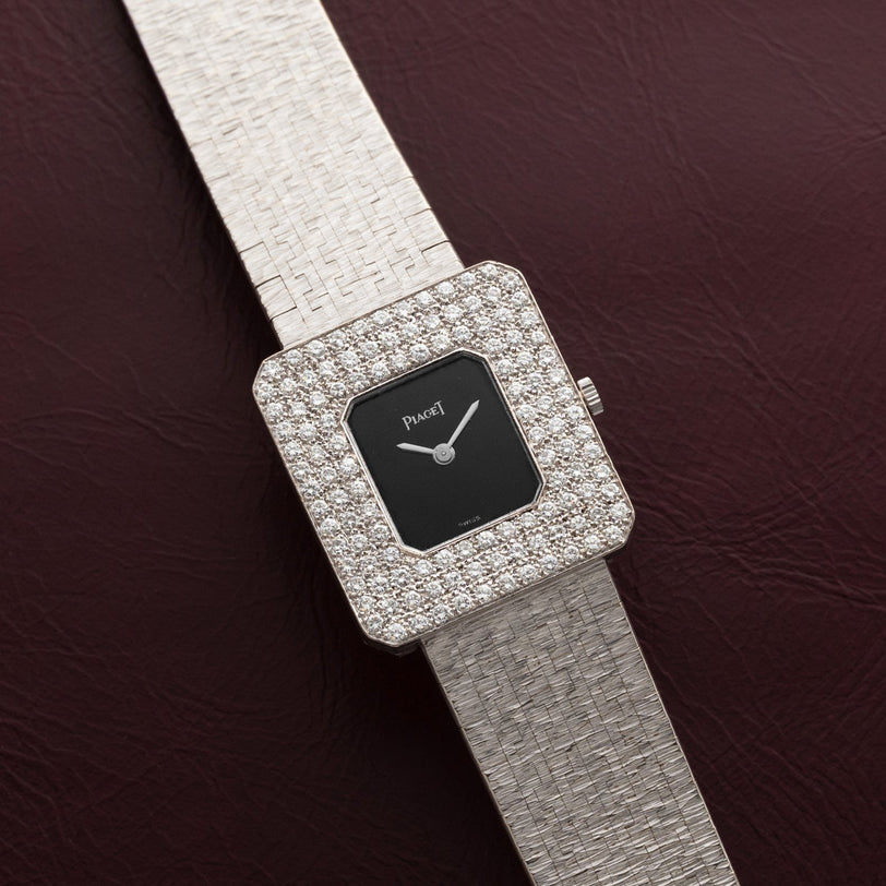 Piaget Onyx Diamond Dress Watch featuring a square face, textured silver band, and diamond-encrusted bezel, displayed on a dark red surface.