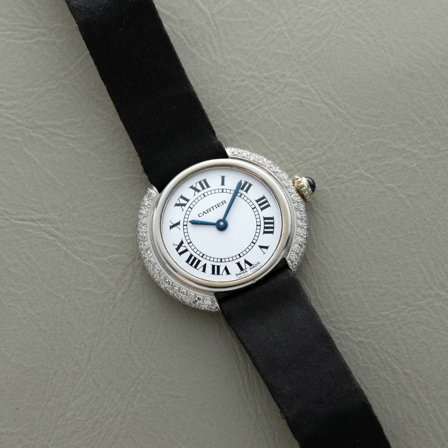 The Cartier Vendome Diamond watch features a black strap, diamond bezel, and Roman numerals on a light gray textured surface.